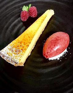 A lemon tart on a black plate with berries